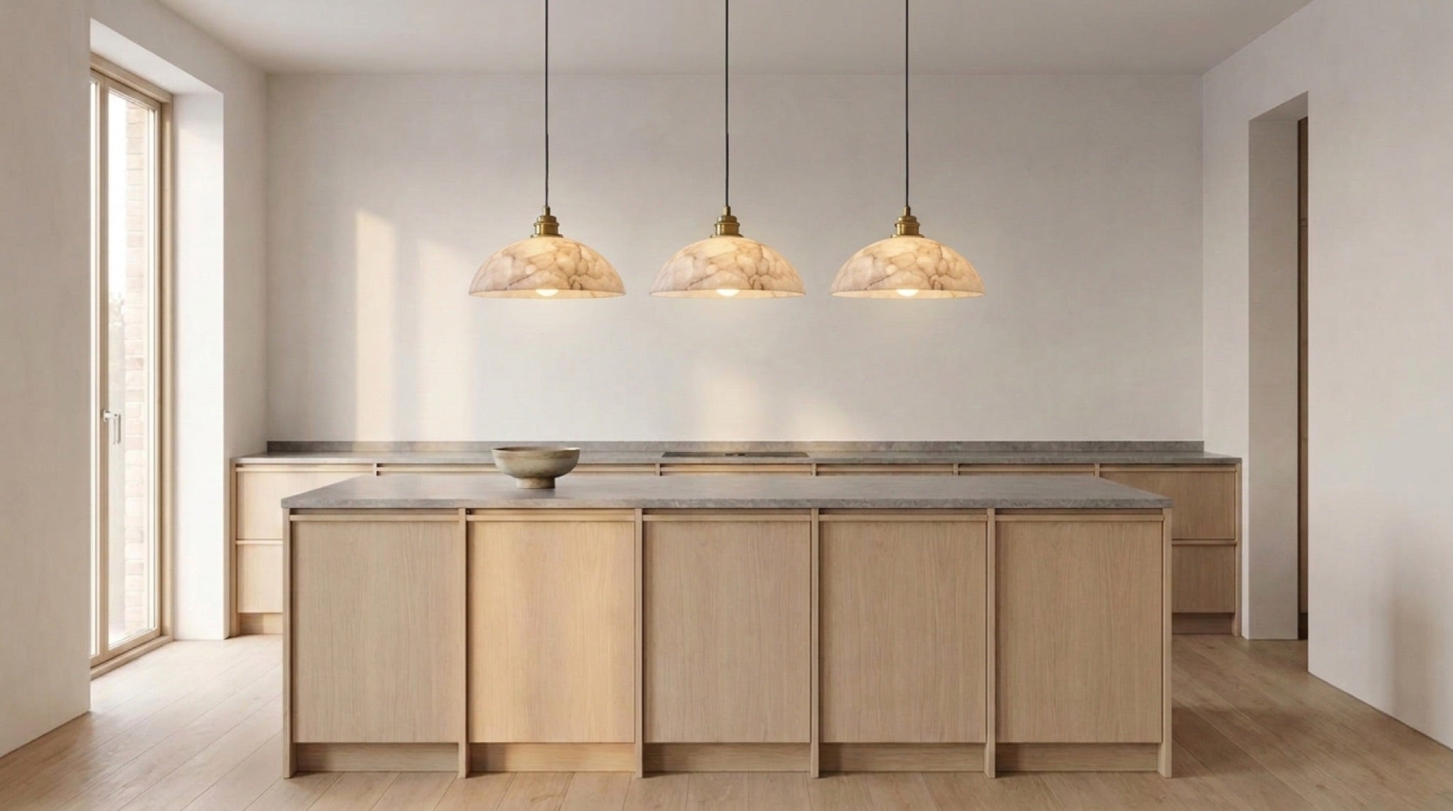 Three alabaster dome pendant lights over a kitchen island in afternoon light